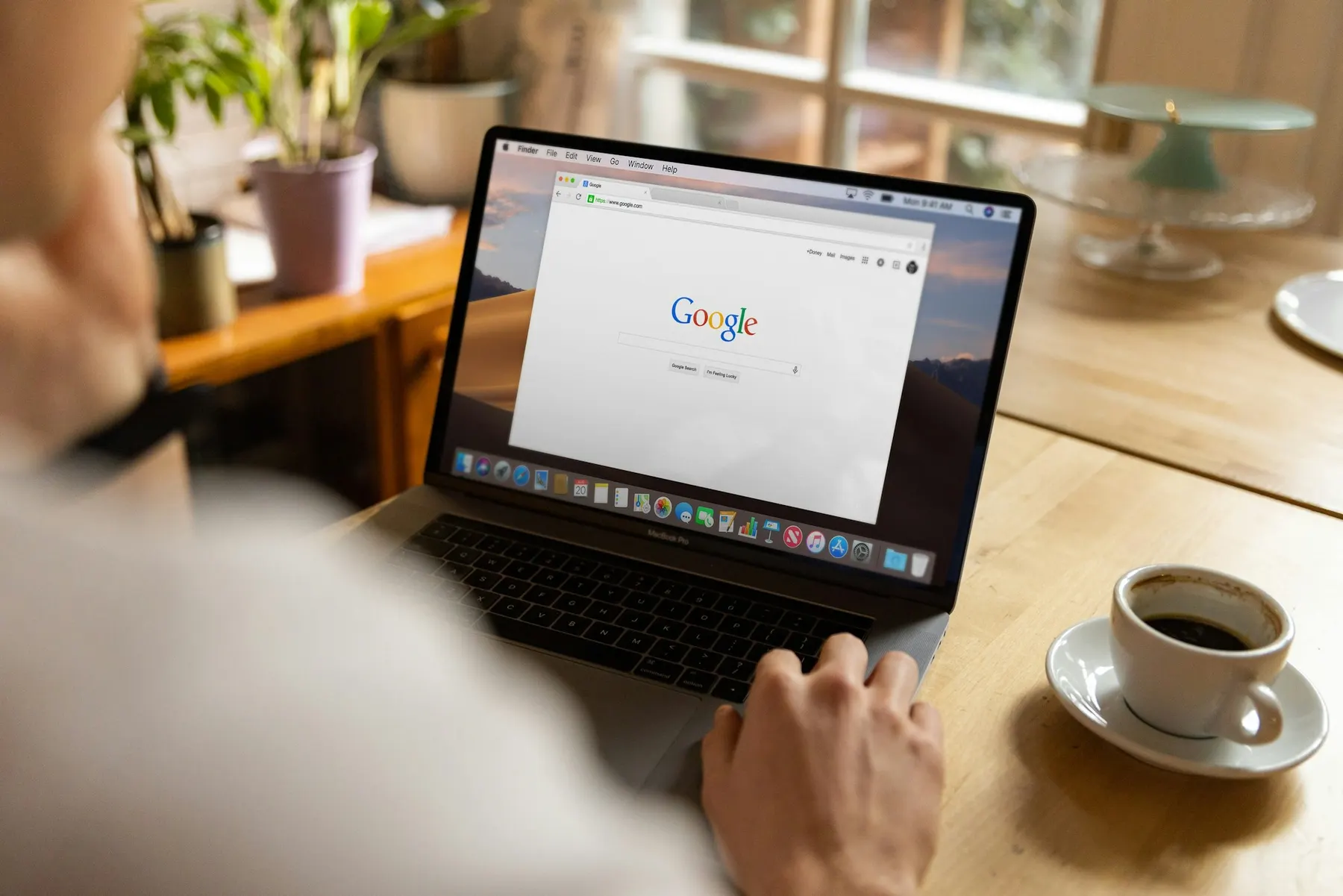 Person at a kitchen table opening Google on a laptop, coffee beside them